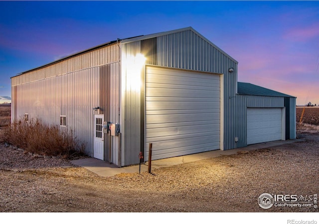 garage at dusk featuring driveway and a detached garage