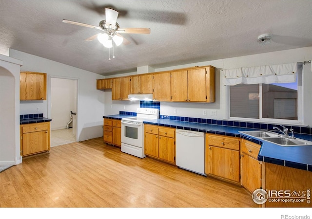 kitchen featuring brown cabinets, light wood-style floors, a sink, white appliances, and under cabinet range hood