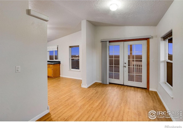 interior space with light wood-style flooring, vaulted ceiling, a textured ceiling, and french doors