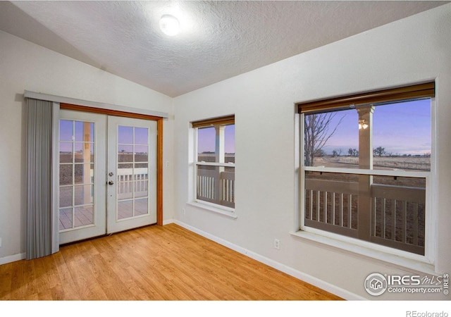 spare room featuring baseboards, lofted ceiling, wood finished floors, a textured ceiling, and french doors