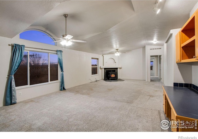 unfurnished living room with vaulted ceiling, a textured ceiling, carpet, and a wood stove