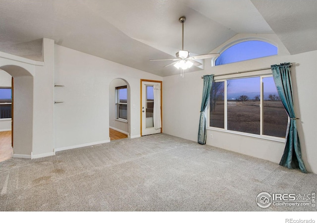 carpeted spare room featuring ceiling fan, arched walkways, and vaulted ceiling