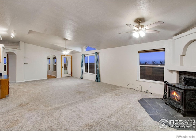 unfurnished living room with arched walkways, a textured ceiling, carpet floors, a ceiling fan, and vaulted ceiling