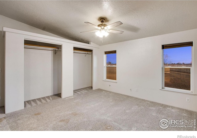 unfurnished bedroom with a textured ceiling, carpet flooring, a ceiling fan, and multiple closets