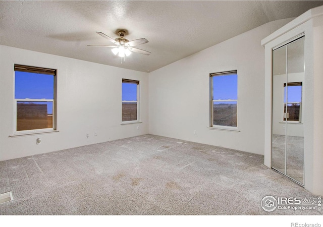 unfurnished room with a textured ceiling, carpet, lofted ceiling, and a ceiling fan