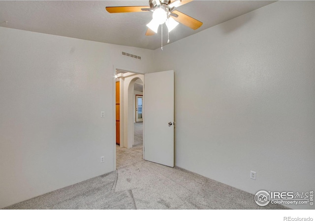 carpeted spare room featuring visible vents, arched walkways, and a ceiling fan