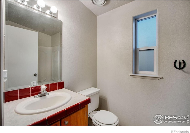 bathroom with a textured wall, vanity, and toilet