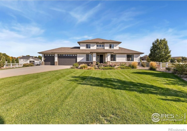 prairie-style home featuring a garage, fence, driveway, stucco siding, and a front lawn