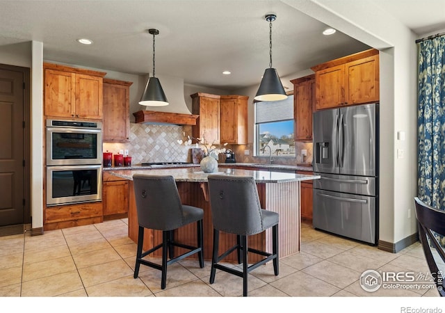 kitchen with stainless steel appliances, brown cabinetry, custom range hood, and light tile patterned floors