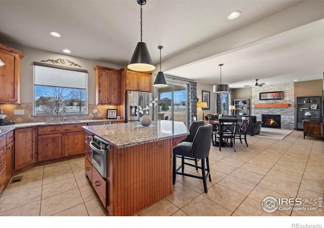 kitchen with light tile patterned flooring, a sink, appliances with stainless steel finishes, backsplash, and decorative light fixtures