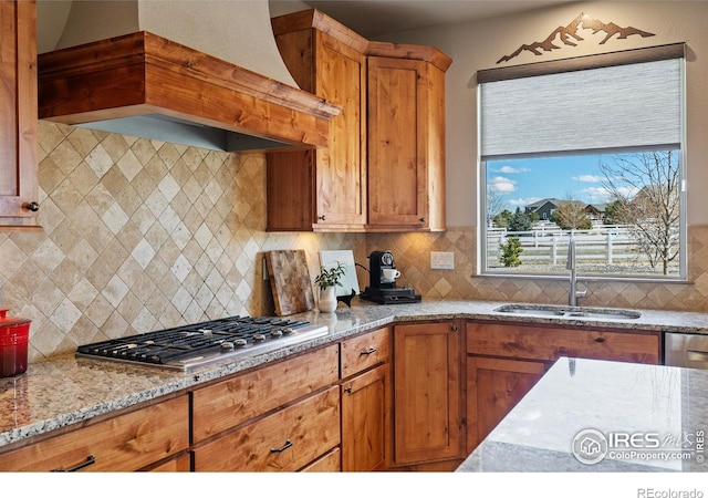 kitchen featuring light stone countertops, stainless steel gas cooktop, a sink, decorative backsplash, and custom range hood