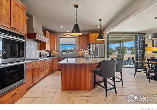 kitchen featuring stainless steel appliances, a kitchen island, brown cabinets, decorative backsplash, and custom range hood