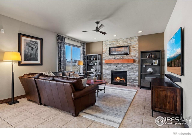 living area with tile patterned floors, baseboards, a ceiling fan, and a stone fireplace