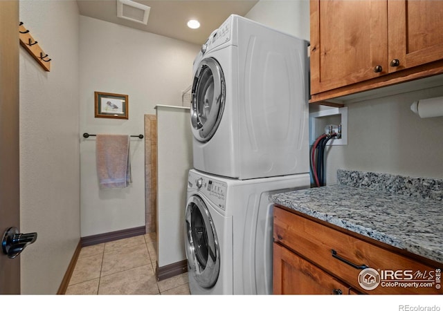 clothes washing area featuring light tile patterned floors, stacked washer and dryer, visible vents, cabinet space, and baseboards