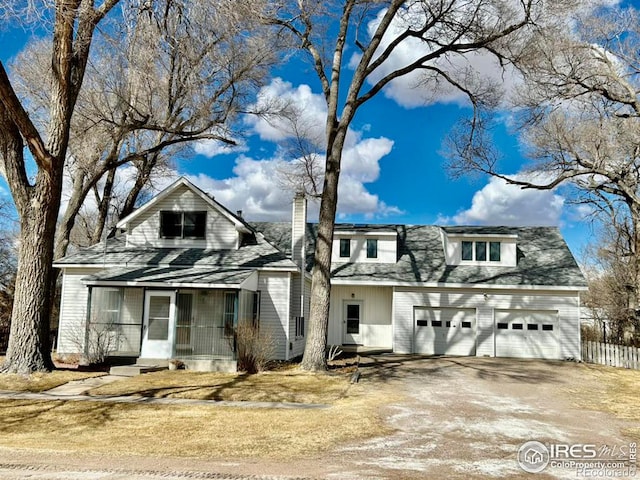 view of front of property with driveway, a garage, a sunroom, a chimney, and fence