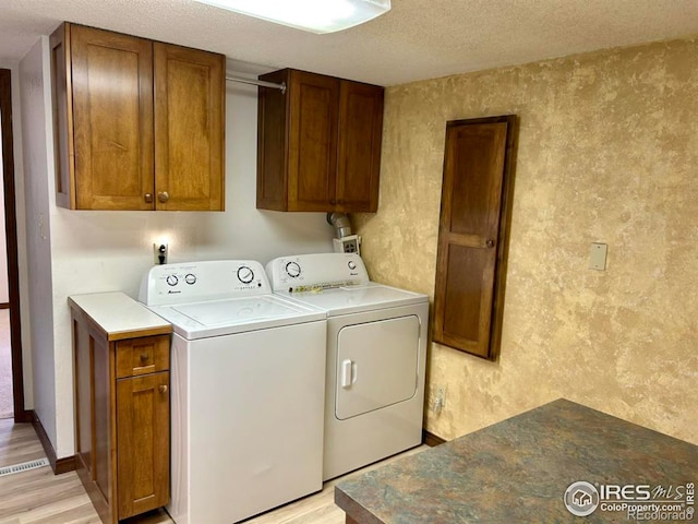 washroom featuring cabinet space, a textured ceiling, washer and clothes dryer, and light wood finished floors