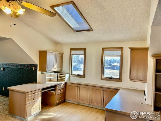 kitchen featuring lofted ceiling with skylight, light wood finished floors, a textured ceiling, and light countertops