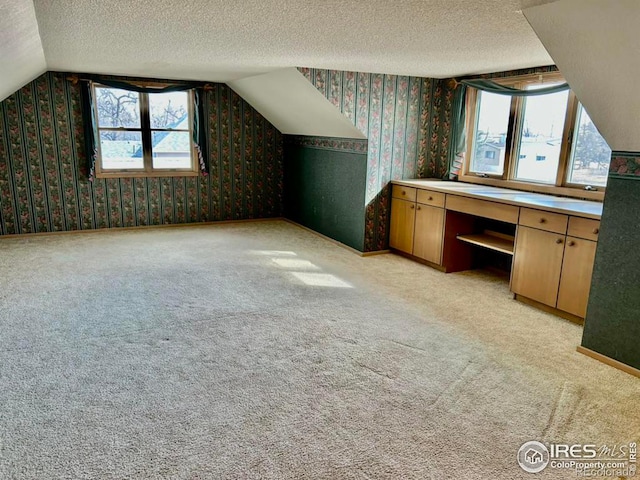 additional living space with lofted ceiling, wallpapered walls, a textured ceiling, and light colored carpet