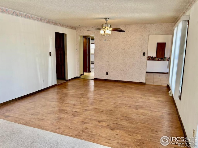 unfurnished room with plenty of natural light, baseboards, a ceiling fan, wood finished floors, and a textured ceiling