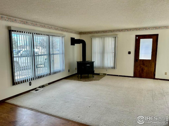 unfurnished living room featuring visible vents, a wood stove, a textured ceiling, wood finished floors, and baseboards