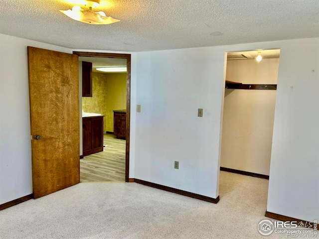 empty room with light carpet, a textured ceiling, and baseboards