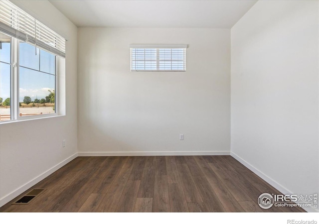 spare room with dark wood-style floors, plenty of natural light, visible vents, and baseboards