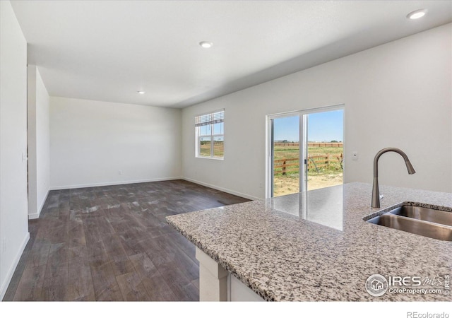 kitchen with light stone counters, dark wood-type flooring, a sink, and baseboards