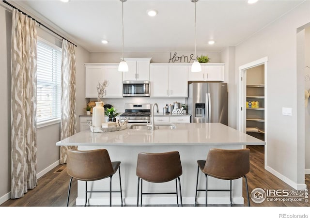 kitchen featuring dark wood finished floors, stainless steel appliances, a breakfast bar, a sink, and baseboards