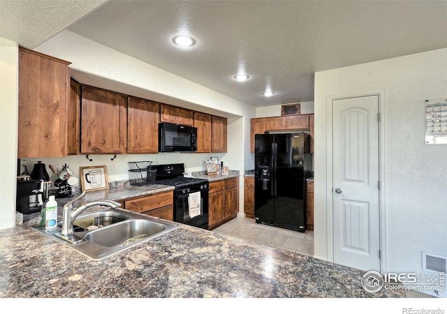 kitchen with dark countertops, brown cabinets, a sink, and black appliances