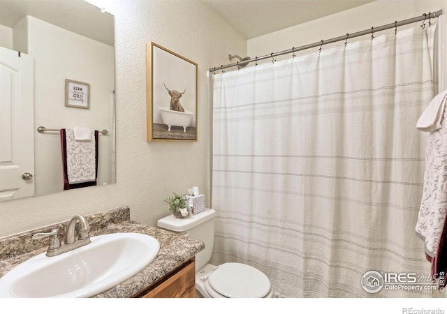 bathroom featuring toilet, a textured wall, and vanity