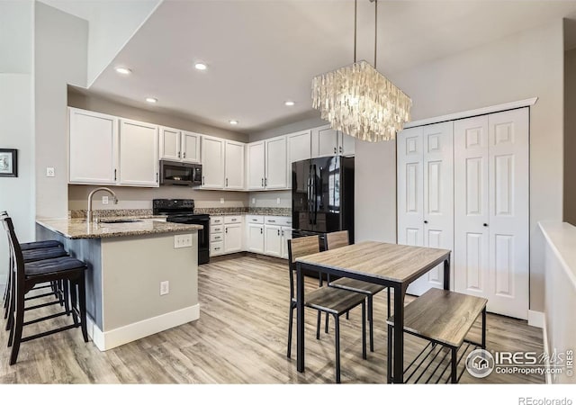 kitchen with a peninsula, a sink, white cabinets, light wood-style floors, and black appliances