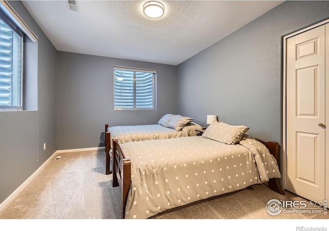 carpeted bedroom featuring a textured ceiling, visible vents, and baseboards