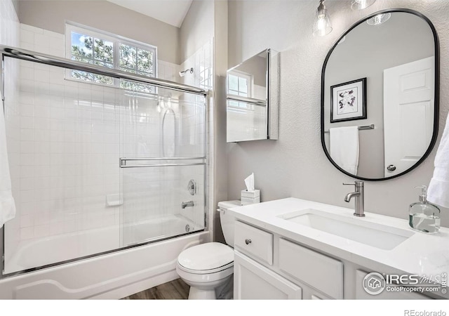 full bath featuring wood finished floors, combined bath / shower with glass door, vanity, and toilet