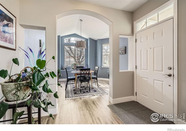 entrance foyer featuring lofted ceiling, baseboards, arched walkways, and wood finished floors