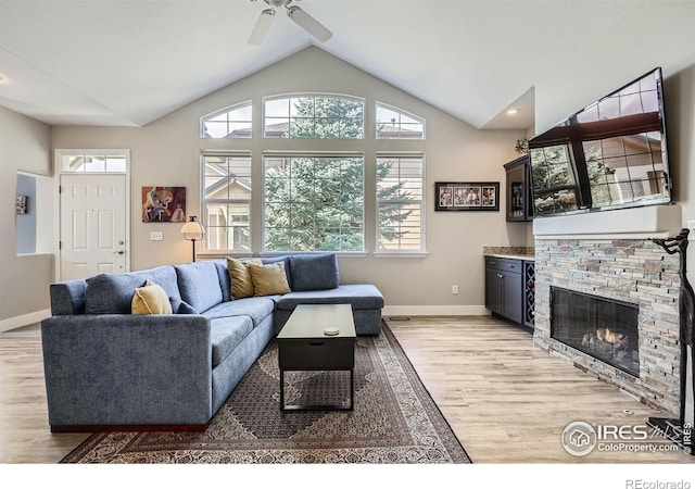 living area with lofted ceiling, light wood-style flooring, baseboards, and a stone fireplace