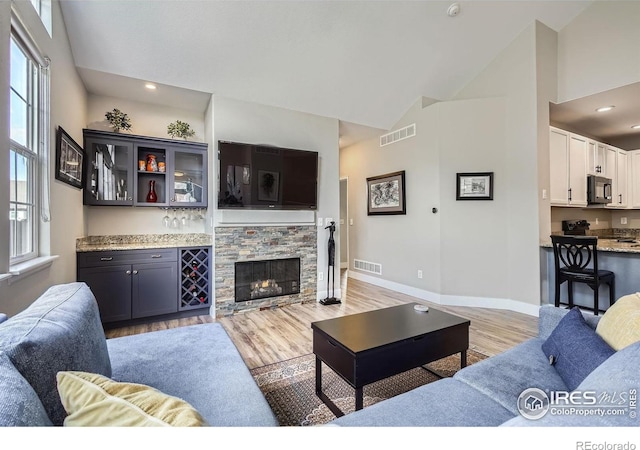 living area featuring light wood-type flooring, a fireplace, visible vents, and baseboards