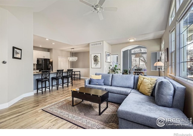 living area with light wood finished floors, baseboards, visible vents, a ceiling fan, and high vaulted ceiling