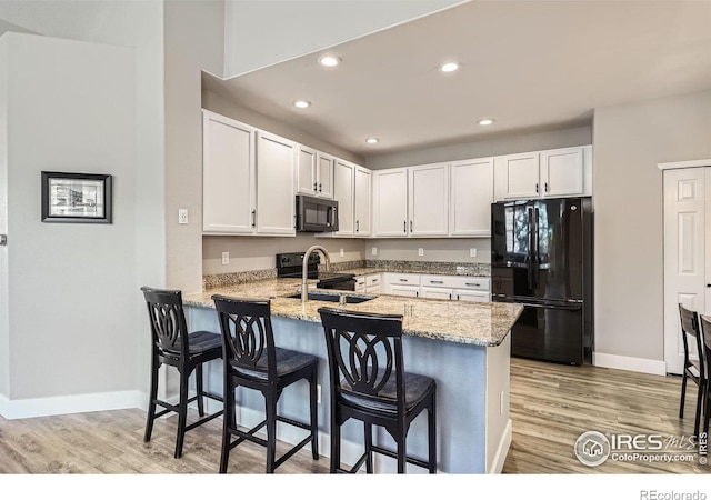 kitchen featuring white cabinets, a sink, light stone countertops, a peninsula, and black appliances