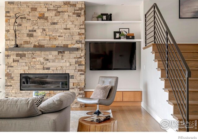 living room with stairs, baseboards, wood finished floors, and a stone fireplace