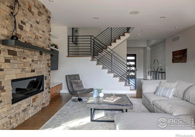 living area featuring a stone fireplace, recessed lighting, visible vents, stairway, and dark wood finished floors