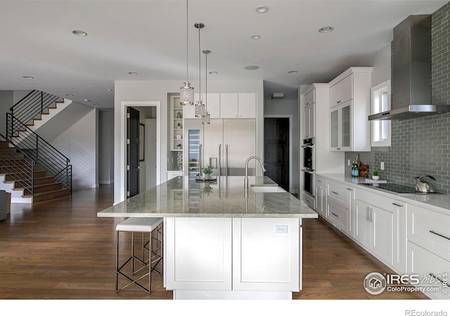 kitchen with black electric cooktop, built in refrigerator, a sink, wall chimney range hood, and dark wood-style floors