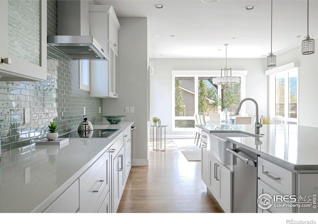 kitchen with decorative backsplash, wood finished floors, black electric stovetop, wall chimney range hood, and stainless steel dishwasher