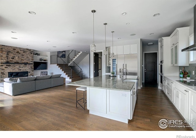 kitchen featuring a breakfast bar, wall chimney exhaust hood, dark wood-type flooring, and a sink