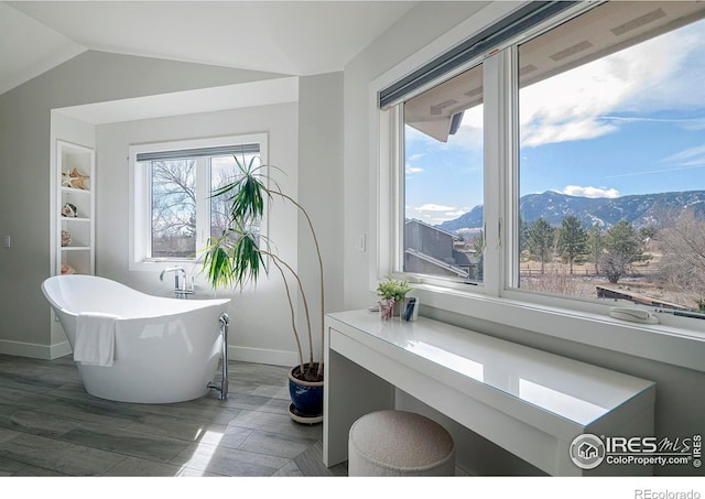 bathroom with lofted ceiling, a freestanding tub, a mountain view, and baseboards