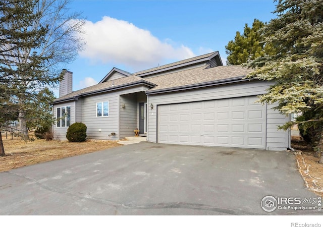 ranch-style home featuring a garage, driveway, a chimney, and a shingled roof