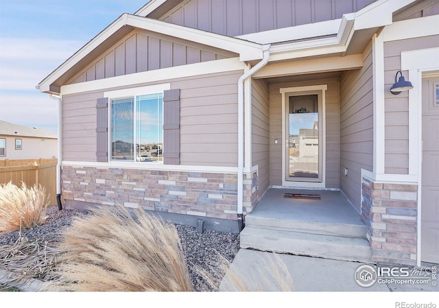 doorway to property featuring board and batten siding, stone siding, and fence