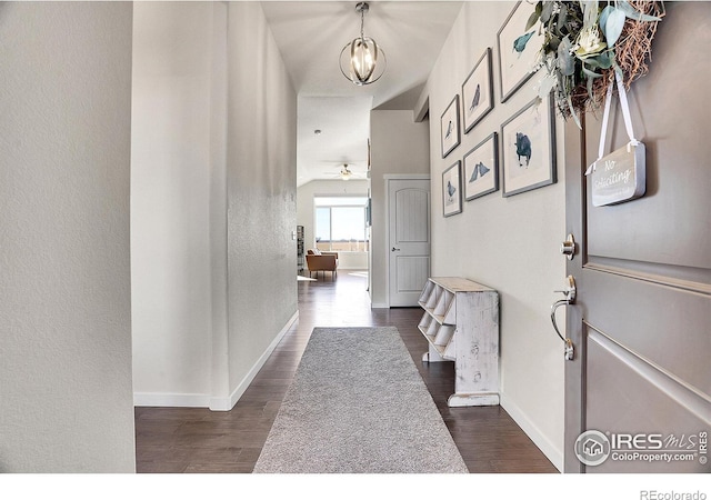 hallway featuring an inviting chandelier, baseboards, and dark wood-type flooring