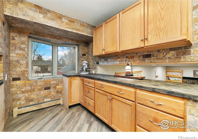 kitchen with dark countertops, brick wall, light wood-style flooring, baseboard heating, and a textured ceiling