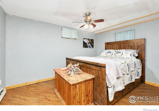 bedroom featuring ceiling fan, a textured ceiling, baseboards, and wood finished floors