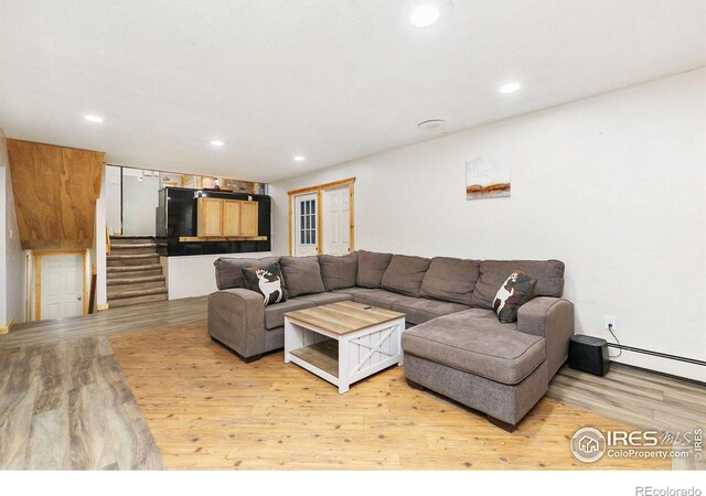 living room featuring recessed lighting, baseboard heating, light wood finished floors, and stairs